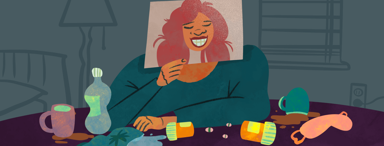 Woman sitting at desk full of pills, an eye mask, and beverages holds up a fake happy photograph