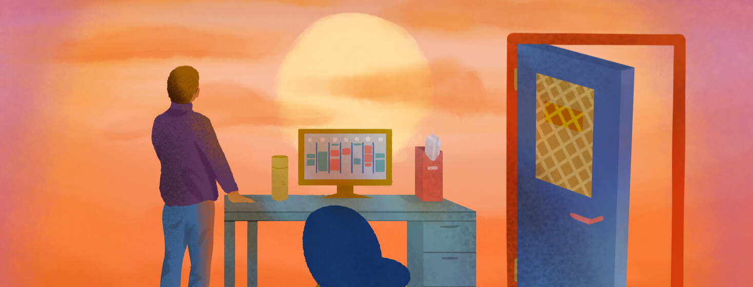 A man from behind in an open office space stares wistfully at a sunset coming down over his desk