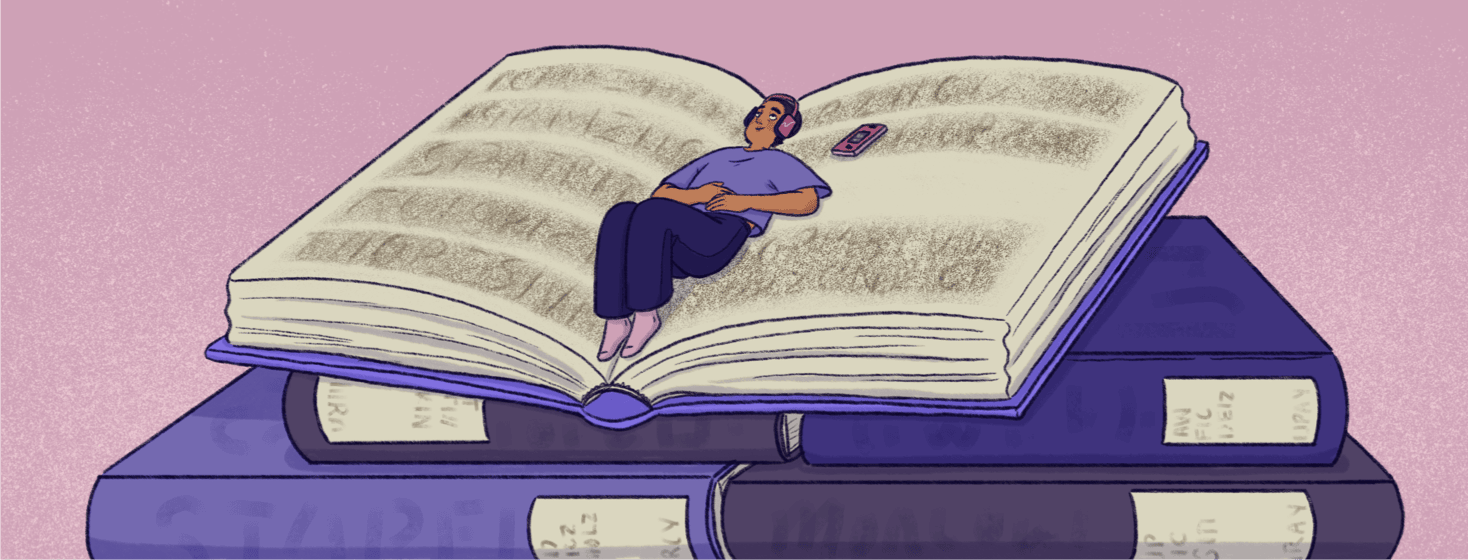 A person has headphones on with their phone next to them; they are lounging in the spine of a giant open book that is on top of a stack of giant library books